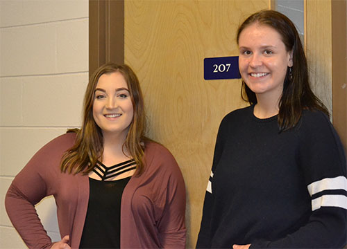 Shanae Fyke (left) and Jenessa Greer (right) pose in front of room 207 in Luther College, where they met in a Women and Gender Studies class. Photo by Jayda Noyes.